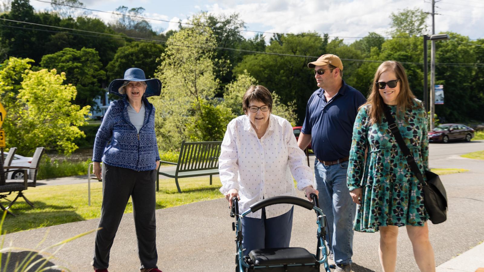 A man and woman dropping off a senior using a walker.